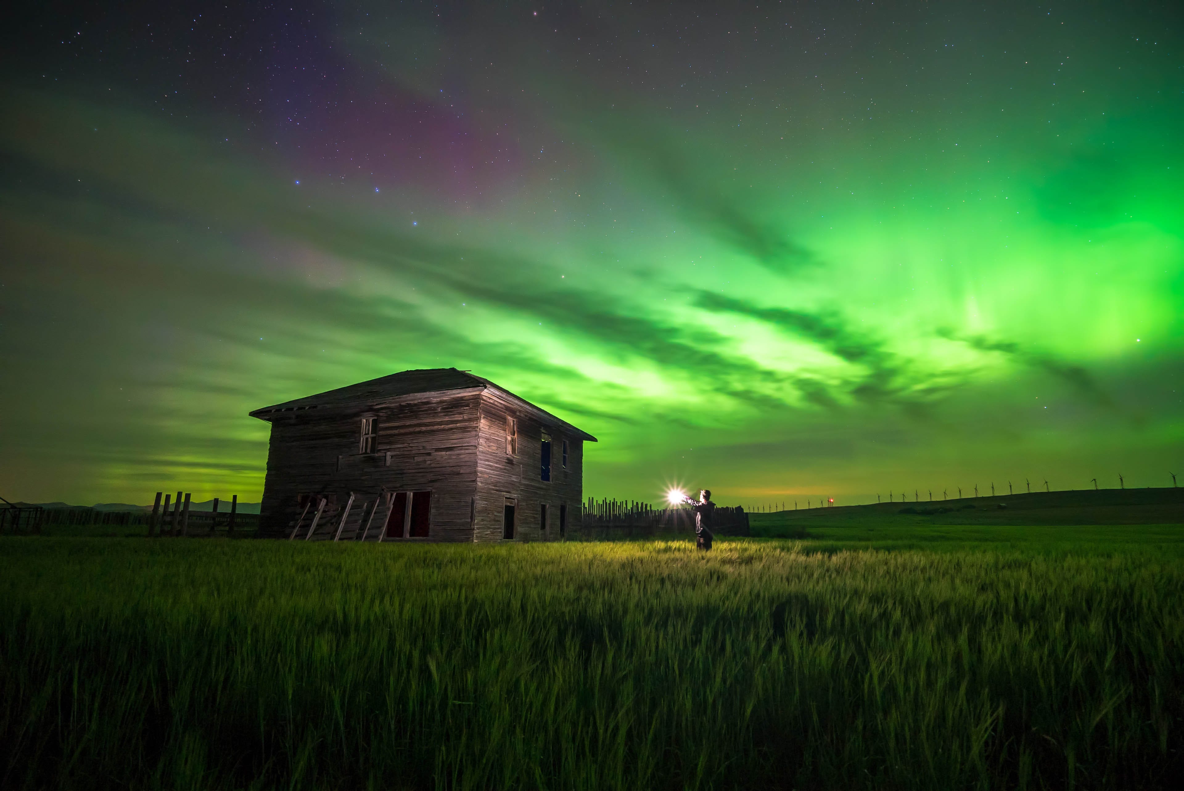 Night shot of a photographer lighting up an abandoned building with the Northern Lights overhead.