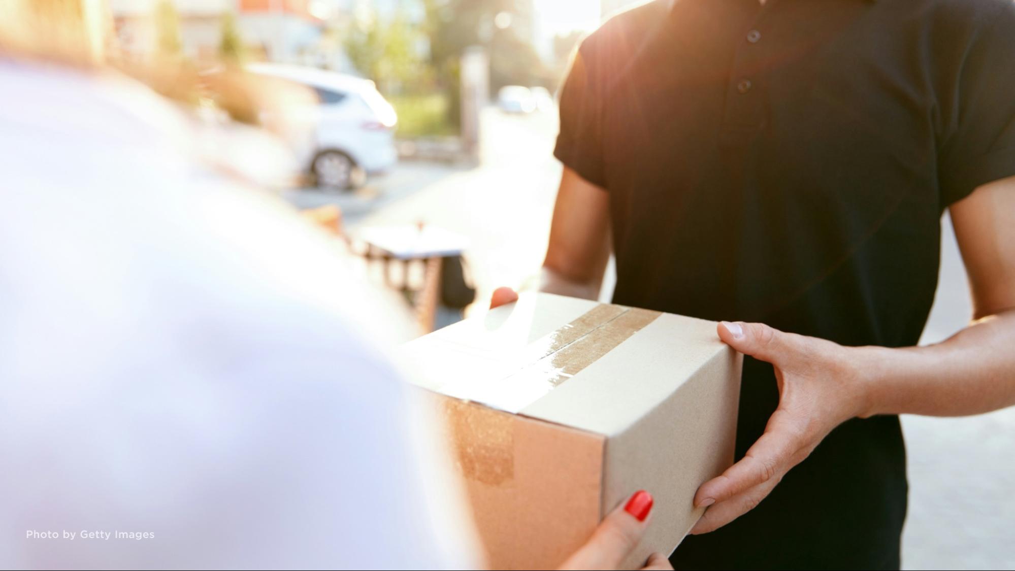 Close-up of a man handing a woman a brown shipping box.