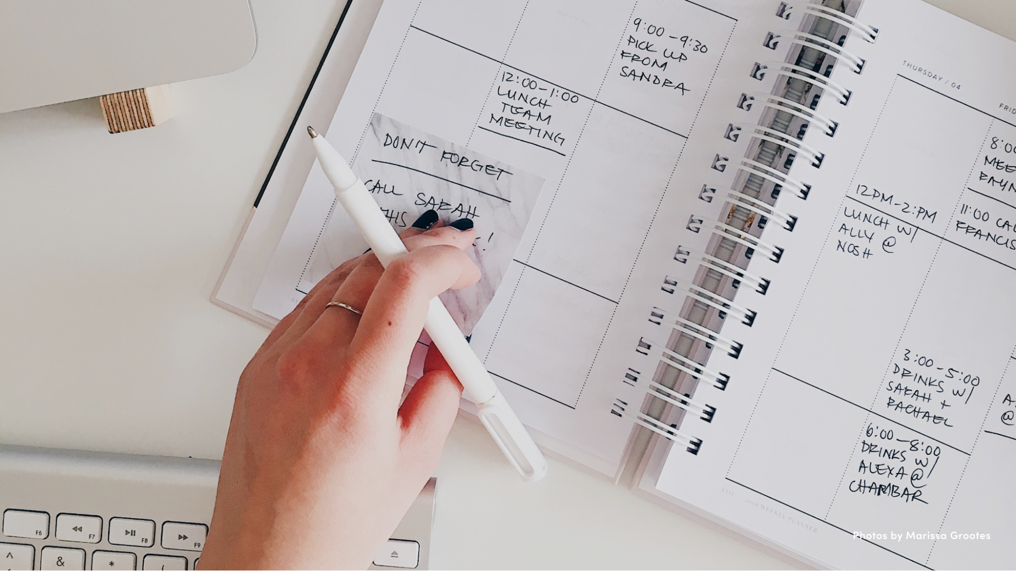 Hand holding a pen and placing a sticky note on a personal calendar.